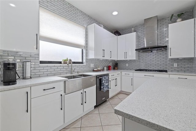 kitchen featuring light tile patterned flooring, wall chimney range hood, tasteful backsplash, a sink, and dishwasher