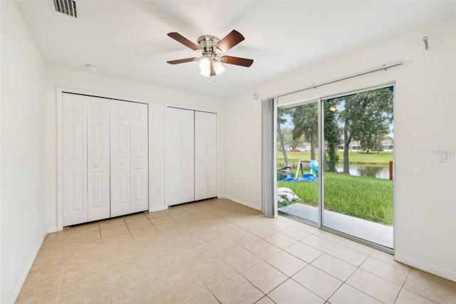 unfurnished bedroom with a water view, access to outside, light tile patterned floors, ceiling fan, and two closets