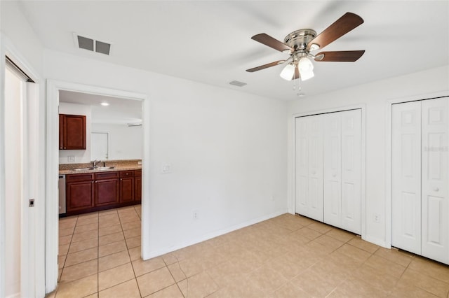 unfurnished bedroom with two closets, ceiling fan, light tile patterned floors, and ensuite bathroom