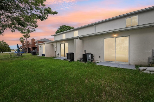 back house at dusk featuring cooling unit, a lawn, and a patio area