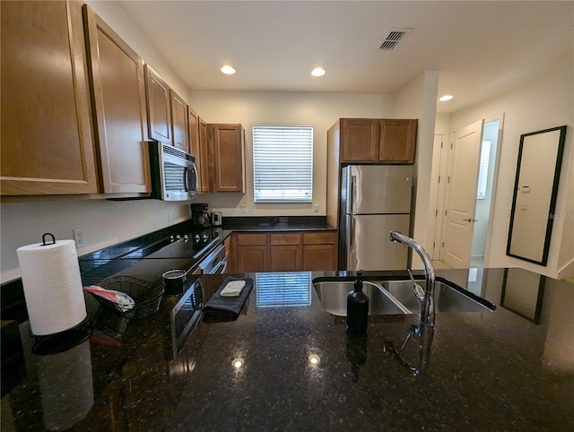 kitchen featuring appliances with stainless steel finishes, dark stone countertops, and sink