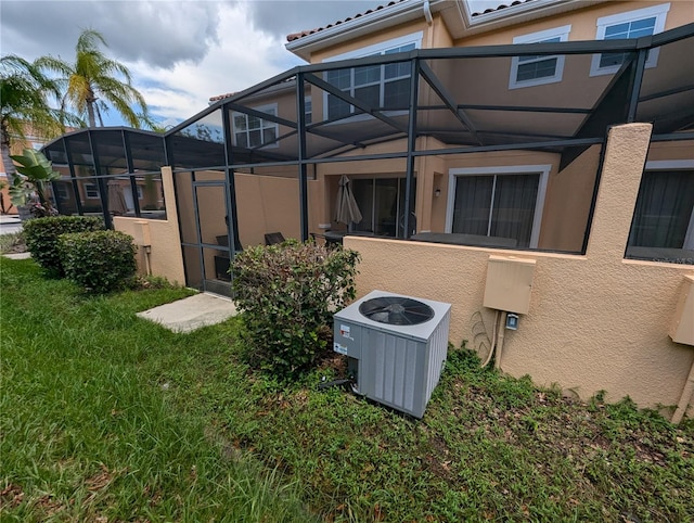 rear view of house featuring glass enclosure, a lawn, and central AC unit