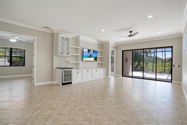 unfurnished living room featuring ceiling fan, built in features, a textured ceiling, beverage cooler, and crown molding