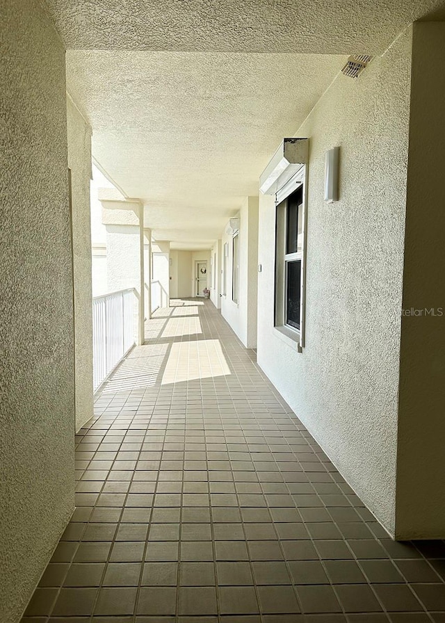 hall with a textured wall, a textured ceiling, and tile patterned floors