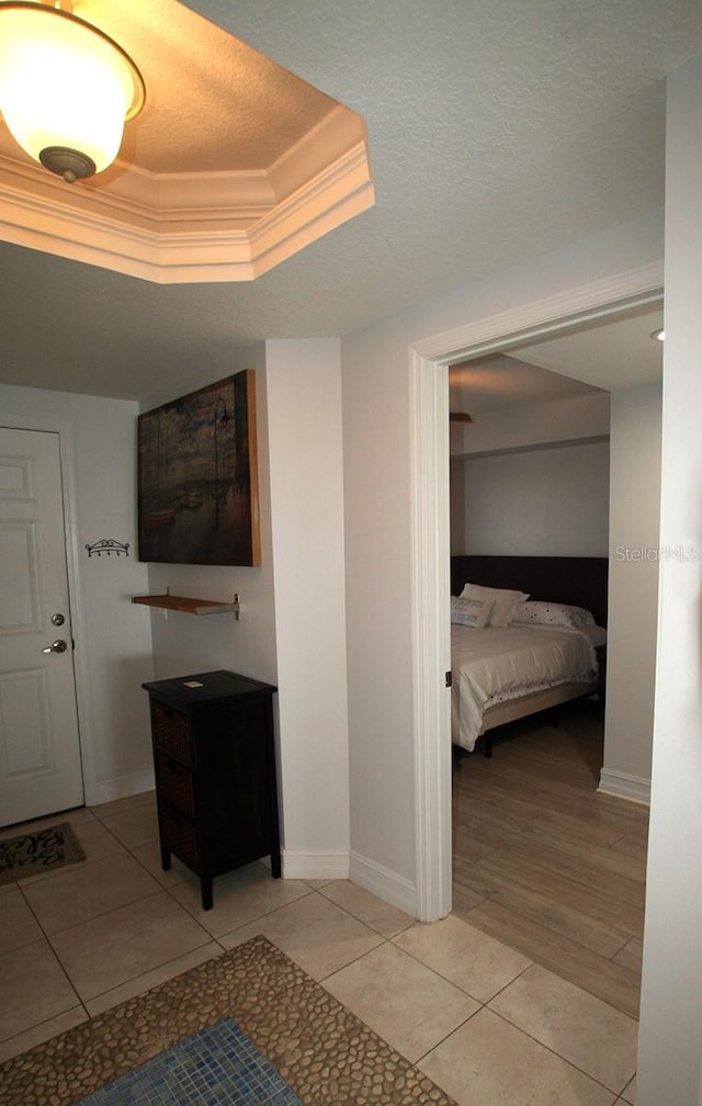 hall featuring light tile patterned floors, a raised ceiling, ornamental molding, a textured ceiling, and baseboards