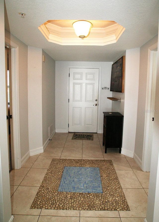 interior space with baseboards, a tray ceiling, ornamental molding, and light tile patterned flooring