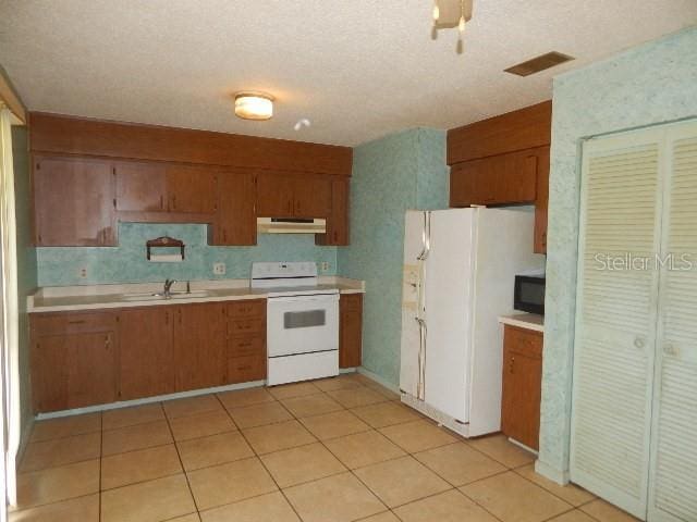 kitchen featuring a textured ceiling, sink, light tile patterned floors, and white appliances