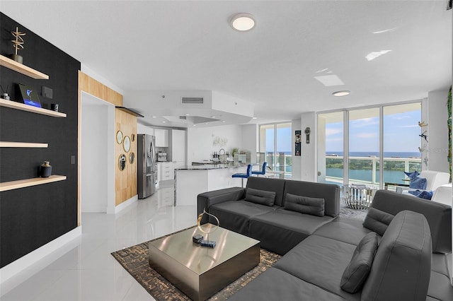 tiled living room featuring a wealth of natural light, sink, expansive windows, and a water view