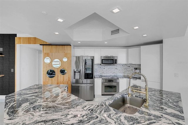 kitchen with stone countertops, backsplash, stainless steel appliances, sink, and white cabinetry