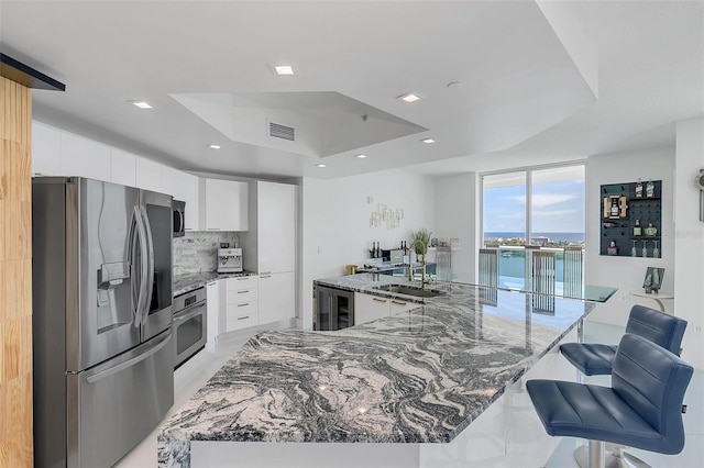 kitchen featuring a raised ceiling, stone countertops, stainless steel appliances, decorative backsplash, and white cabinetry