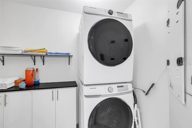 washroom with stacked washer and clothes dryer and cabinets