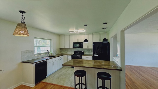 kitchen with light wood-type flooring, a breakfast bar, black appliances, white cabinetry, and butcher block counters