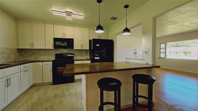 kitchen featuring a breakfast bar, black appliances, white cabinets, hanging light fixtures, and butcher block counters