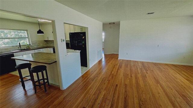 kitchen with light wood-type flooring, a breakfast bar, black appliances, decorative light fixtures, and white cabinetry