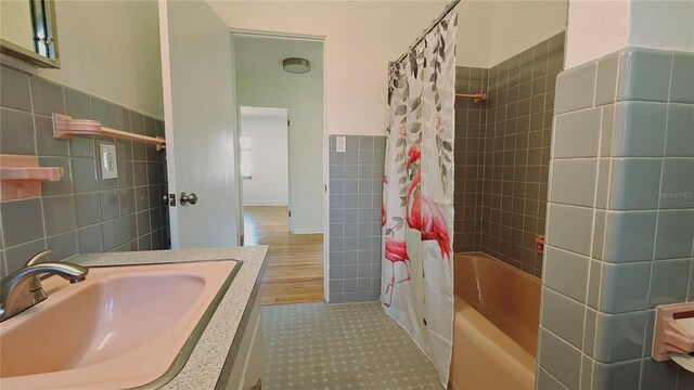 bathroom featuring wood-type flooring, vanity, tile walls, and shower / bath combo with shower curtain