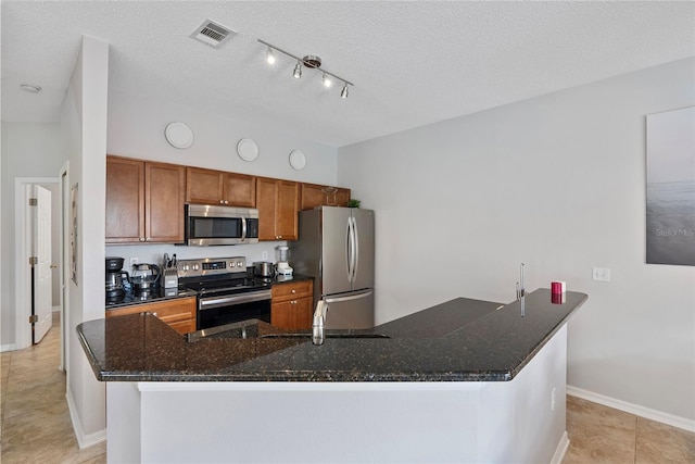 kitchen with a textured ceiling, light tile patterned flooring, dark stone countertops, and stainless steel appliances