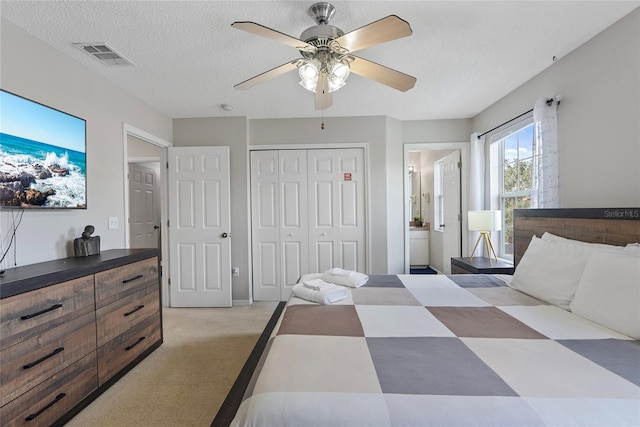 carpeted bedroom with ceiling fan, a closet, ensuite bathroom, and a textured ceiling