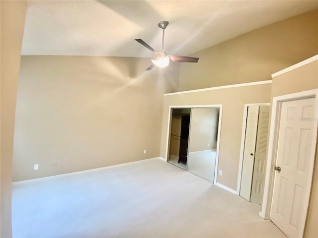 unfurnished bedroom with lofted ceiling, light colored carpet, ceiling fan, and multiple closets