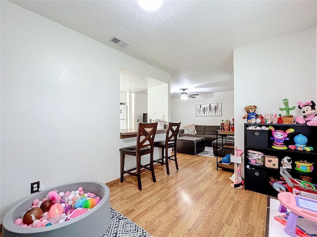 playroom with a textured ceiling, light hardwood / wood-style flooring, and ceiling fan