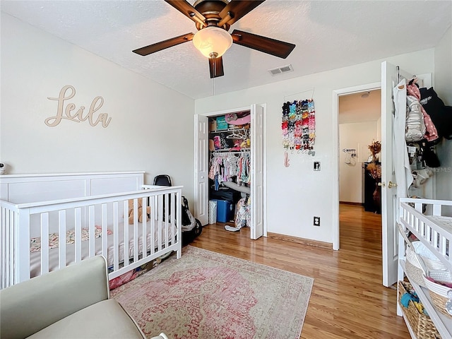 bedroom with a textured ceiling, a nursery area, ceiling fan, and light hardwood / wood-style flooring