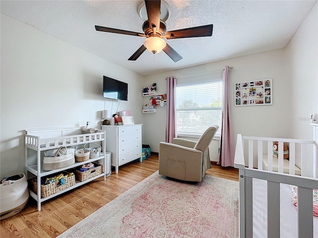 bedroom with a textured ceiling, light hardwood / wood-style flooring, ceiling fan, and a crib