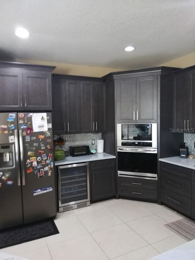 kitchen featuring light tile patterned floors, appliances with stainless steel finishes, wine cooler, decorative backsplash, and a textured ceiling