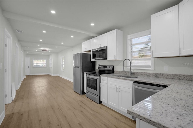 kitchen featuring stainless steel appliances, plenty of natural light, sink, light stone countertops, and light hardwood / wood-style floors