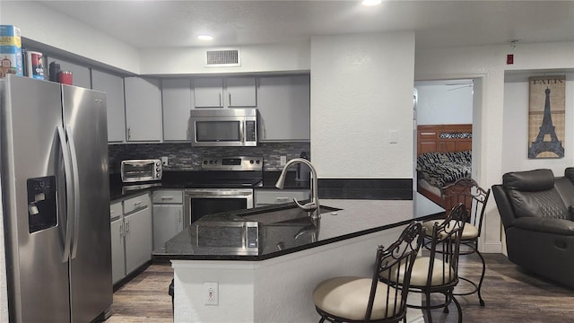 kitchen featuring gray cabinetry, dark hardwood / wood-style floors, stainless steel appliances, kitchen peninsula, and sink