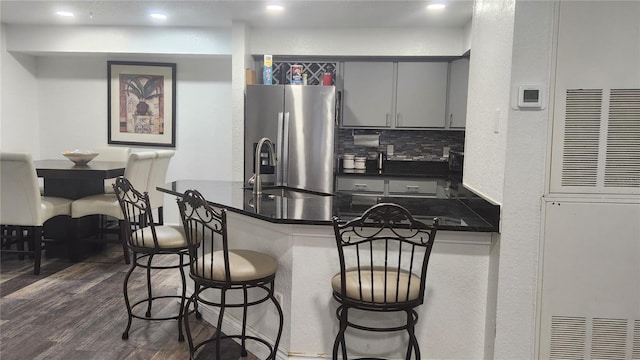 kitchen featuring dark hardwood / wood-style floors, a kitchen breakfast bar, stainless steel fridge, kitchen peninsula, and decorative backsplash