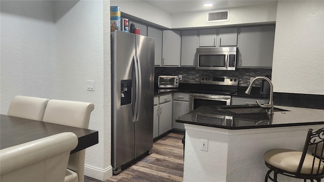 kitchen with gray cabinets, tasteful backsplash, stainless steel appliances, kitchen peninsula, and sink