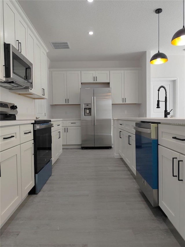 kitchen featuring a textured ceiling, light hardwood / wood-style flooring, decorative light fixtures, stainless steel appliances, and white cabinets