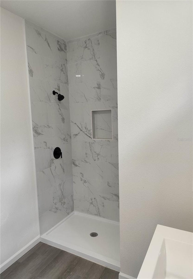 bathroom with a tile shower and wood-type flooring