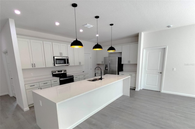 kitchen with light wood-type flooring, appliances with stainless steel finishes, sink, and a center island with sink