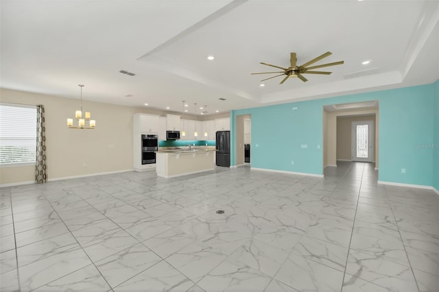 unfurnished living room featuring a tray ceiling and ceiling fan with notable chandelier