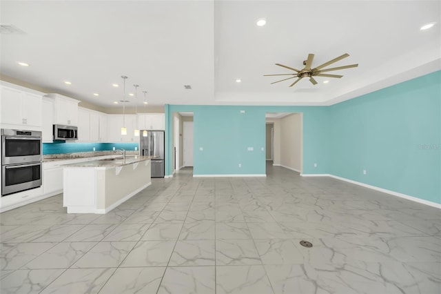 kitchen featuring ceiling fan, hanging light fixtures, appliances with stainless steel finishes, a center island with sink, and white cabinets