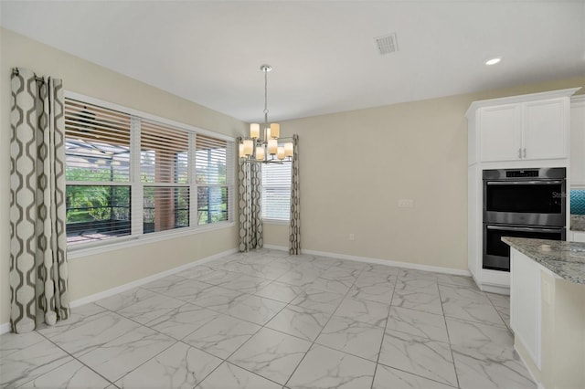 kitchen featuring light stone countertops, decorative light fixtures, white cabinets, a chandelier, and double oven