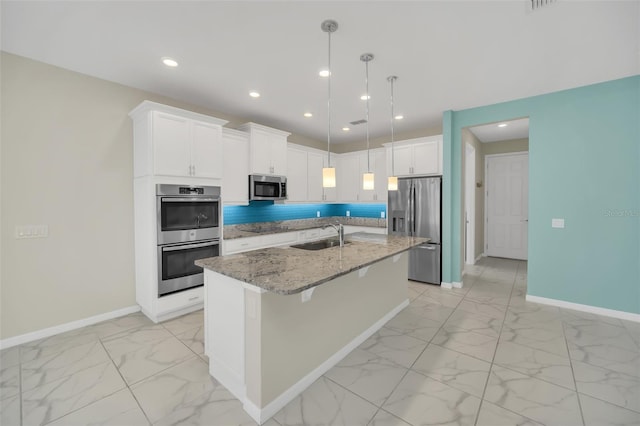 kitchen with appliances with stainless steel finishes, light stone countertops, white cabinetry, sink, and an island with sink