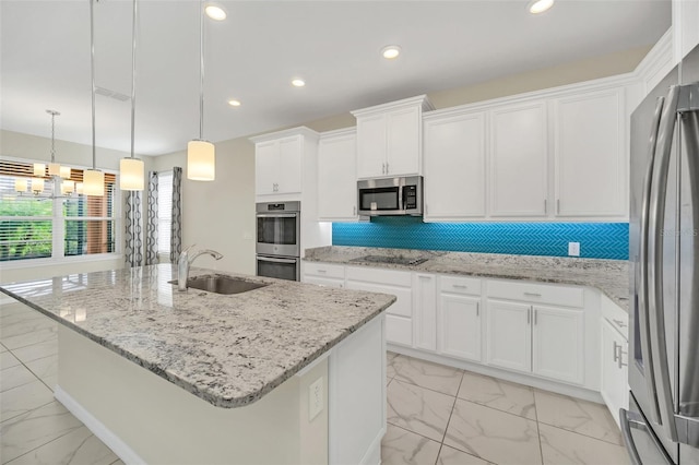 kitchen featuring white cabinetry, backsplash, light stone counters, an island with sink, and appliances with stainless steel finishes