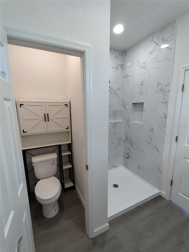 bathroom with hardwood / wood-style floors, toilet, and tiled shower