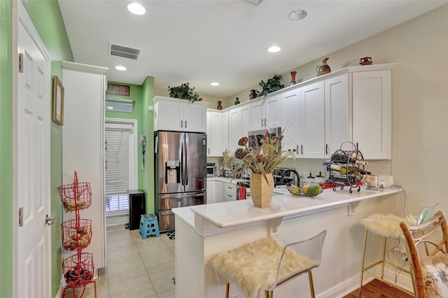 kitchen with a kitchen bar, stainless steel appliances, kitchen peninsula, and white cabinetry