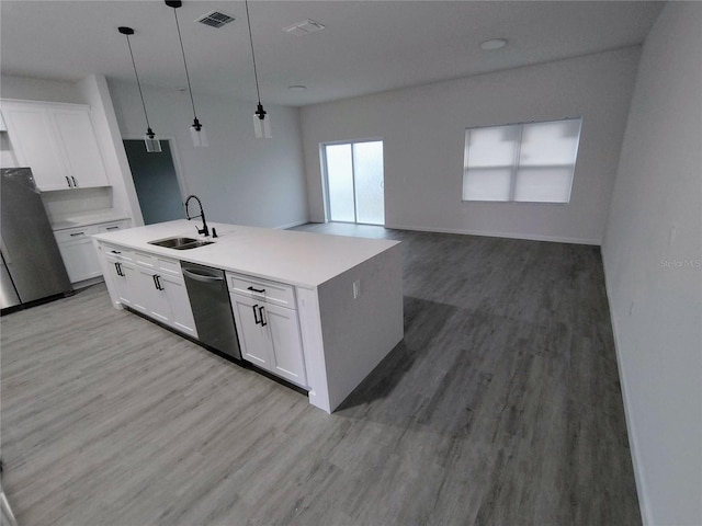 kitchen featuring white cabinets, hanging light fixtures, stainless steel appliances, and a center island with sink