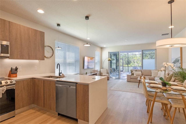 kitchen featuring pendant lighting, stainless steel appliances, kitchen peninsula, sink, and light hardwood / wood-style floors