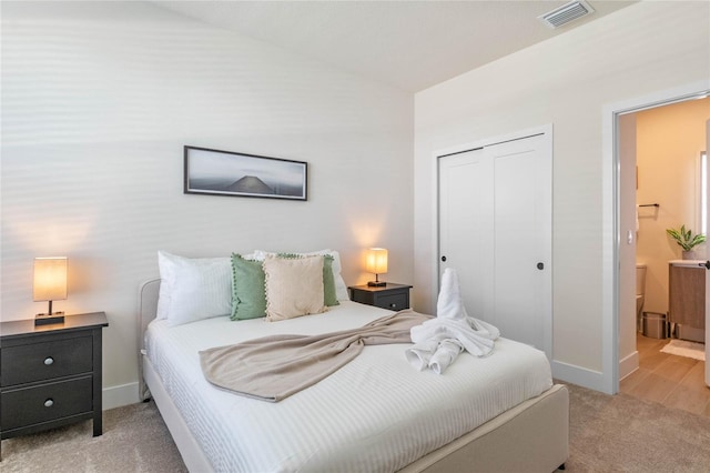 bedroom featuring connected bathroom, light colored carpet, and a closet