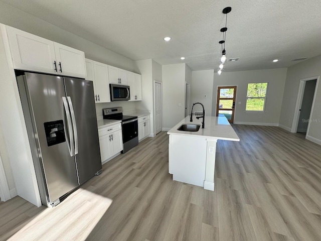 kitchen with a sink, a textured ceiling, stainless steel appliances, white cabinets, and light wood finished floors