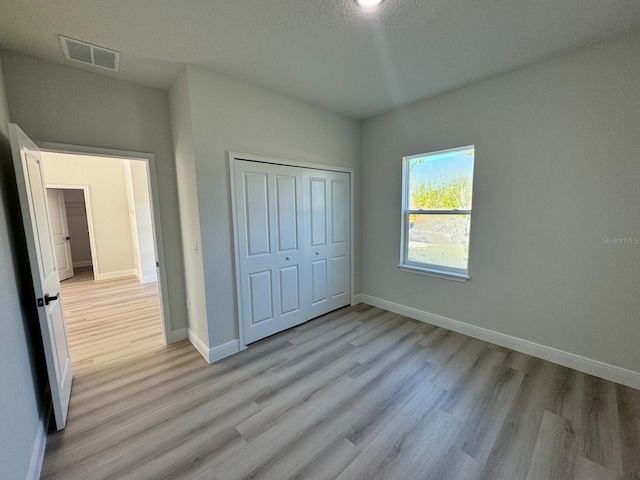 unfurnished bedroom with light wood-style floors, visible vents, a closet, and baseboards