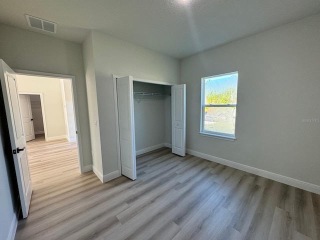 unfurnished bedroom featuring light wood-style flooring, baseboards, visible vents, and a closet