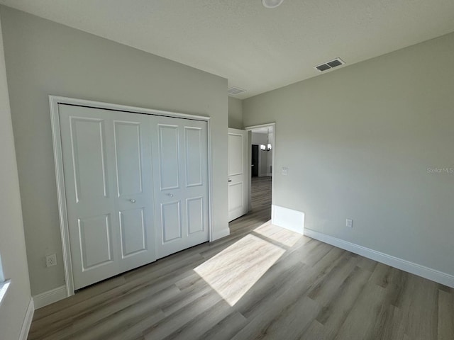 unfurnished bedroom with light wood finished floors, visible vents, a closet, and baseboards