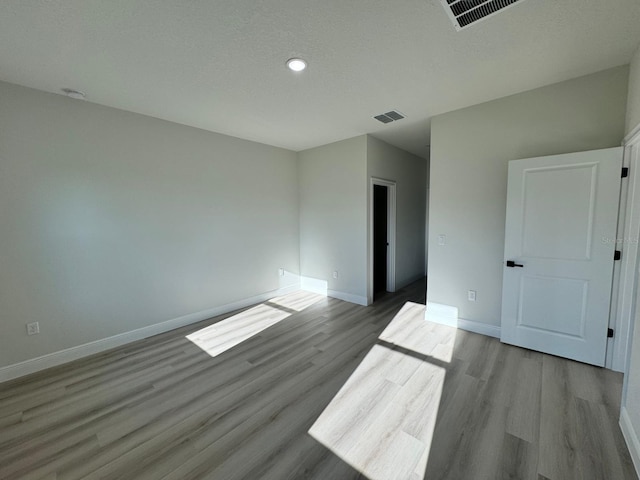 empty room featuring visible vents, a textured ceiling, baseboards, and wood finished floors