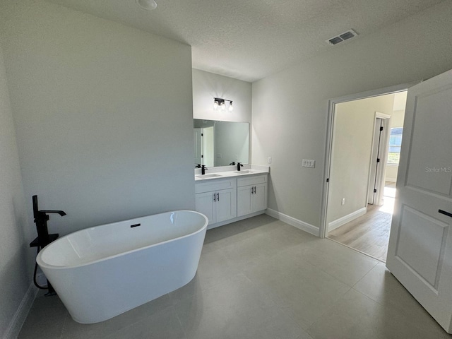 full bath with double vanity, visible vents, a freestanding bath, and a sink