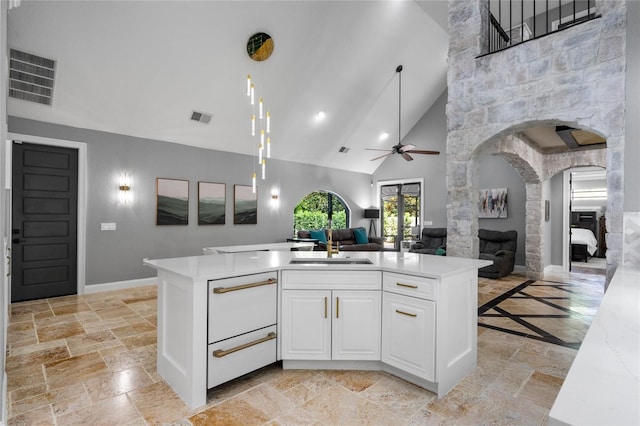 kitchen featuring a stone fireplace, sink, high vaulted ceiling, white cabinetry, and ceiling fan